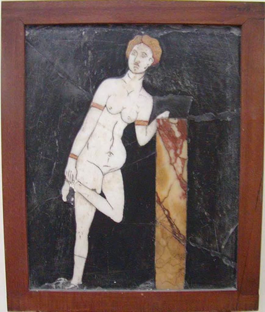 I.2.10 Pompeii. Found in triclinium. 
Black crystalline rock adorned with opus sectile tablet of Venus untying, or doing up, her sandal. 
Now in Naples Archaeological Museum.  Inventory number: 109678.
According to Fiorelli, the triclinium was adorned with paintings that were now non-existent, other than a tablet of schist inserted into the wall.
On the tablet was mounted a marble figure of Venus untying her shoes.
See Pappalardo, U., 2001. La Descrizione di Pompei per Giuseppe Fiorelli (1875). Napoli: Massa Editore. (p.35)
According to Warscher, quoting Olga Elia (Bollettino darte, 1929, p.276)  
Di due pannelli decorativi pompeiani con figure in opus sectile ad intarsio
Qui ci troviamo dinanzi ad un lavoro di ordine inferiore, di valore estetico negativo, per il rendimente del tipo e la trascuratezza della tecnica.
Aggiungo qui un quadretto di opus sectile rinvenuto nella casa 10, of Insula 2, Regione I: vi  rappresentata su fondo nero di pietra di Genova una Venere in marmo bianco, che con capelli e braccialetti di marmo giallo, appoggiandosi con la sinistra ad un pilastrino, solleva la gamba sinistra per porsi al piede un armillo. 
See Warscher T., 1935. Codex Topographicus Pompeianus: Regio I.2. (no.22a), Rome: DAIR. 
