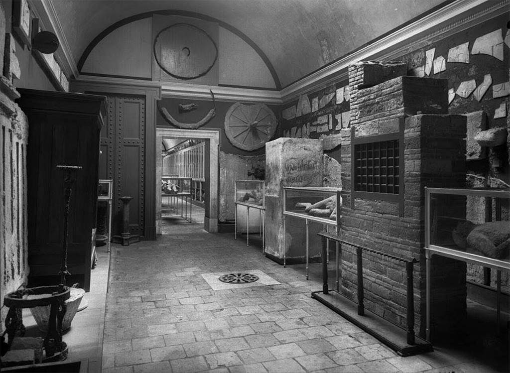 I.3.24 Pompeii. Pre 1943 undated photo showing some of the contents of the antiquarium listed by Fiorelli in his guide.
On the right of the doorway is the cast of the ancient door with locks.
Left of the doorway is the reconstructed door and the reconstructed cupboard. All drawn by Gusman (see above). 
Photo courtesy Dr Sophie Hay.
