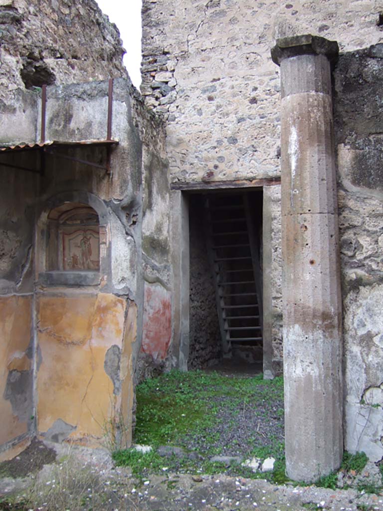 V.2.h Pompeii. December 2005. 
Looking north to doorway from walkway ‘k’, across area ‘h’, to room ‘e’, the corridor, with wooden reconstructed stairs to the upper cenacolo. 
According to NdS, corridor ‘e’ had a threshold of travertine and walls covered with a rustic white plaster.
In the north-west corner of room ‘e’ was a low masonry block, probably the beginning of an ascending stairway.

At the south end of the corridor was a doorway (seen above) leading into area ‘h’, which also had doorways to the tablinum ‘f’, to room ‘i’ a cubiculum, to room ‘l’ triclinium, and doorway to walkway ‘k’ (above) leading to the garden, room ‘n’. 

The small garden ‘n’ was preceded by a walkway ‘k’ protected by a roof, which projected from the roof, which covered room ‘h’.
This walkway had a floor of flagstones, littered with chunks or flakes of marble, and did not show any other decoration other than a high yellow dado on the west wall and in the north-west corner.
See Notizie degli Scavi di Antichità, 1896, (p.423) which refers to walkway ‘h’, across area ‘f’, to corridor ‘c’, with wooden stairs, cubiculum ‘i’, triclinium ’g’, garden ‘l’. 

In the north-west corner of walkway ‘h’, on the north side of the garden, was a lararium niche and column.
According to Boyce, in the garden was found a cylindrical altar of terracotta, around which a serpent coiled, its head raised above the top.
See Boyce G. K., 1937. Corpus of the Lararia of Pompeii. Rome: MAAR 14. (p.36, note 1). 
