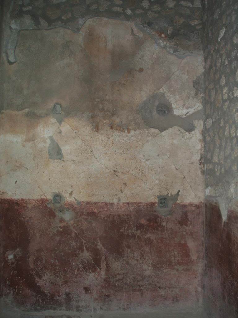 VI.8.23 Pompeii. May 2005. Room on north side of atrium.
Remains of simple wall painting from north wall, a painted red dado (zoccolo) with white painted upper wall but lacking any decoration. 
All around the wall at regular intervals, some holes were drilled for shelving supports. 
