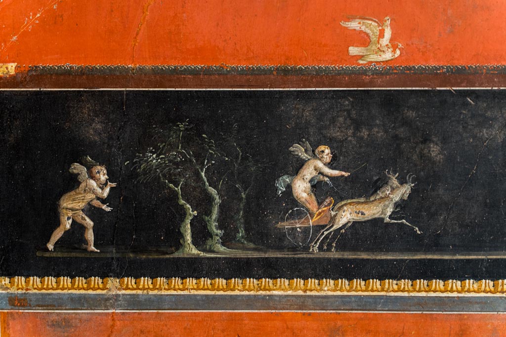 VI.15.1 Pompeii. March 2023. 
Lower centre of east wall, detail of part of painted panel with cupids in a chariot race. Photo courtesy of Johannes Eber.
