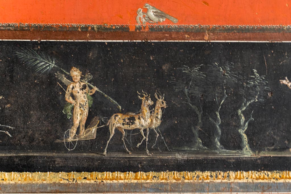 VI.15.1 Pompeii. March 2023. 
Lower centre of east wall, detail of part of painted panel  - the winning cupid in chariot race. Photo courtesy of Johannes Eber.
