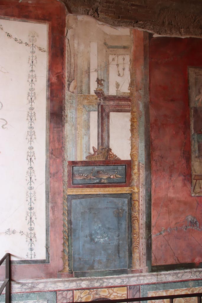 VI.15.1 Pompeii. October 2023.  
North wall of exedra on west side of central painting, wall painting of naval scene, with basket and mask above.
Photo courtesy of Klaus Heese.
