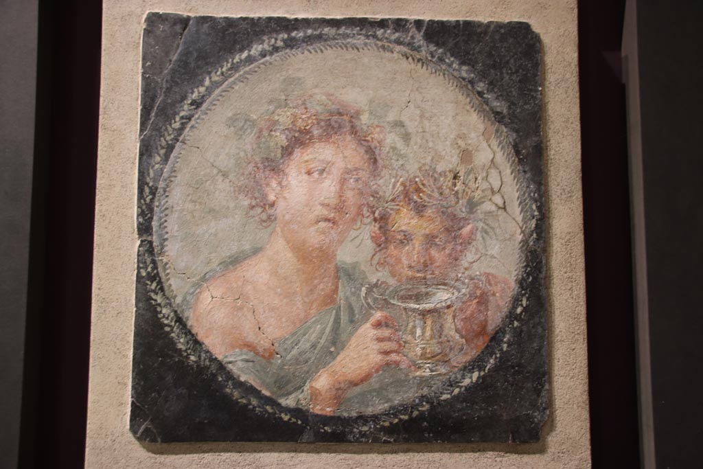 VI.17.42 Pompeii. October 2022. Medallion depicting Maenad and a young Satyr holding a silver drinking cup for wine (a kantharos). 
Found at the west end of the north wall of the large triclinium with a vaulted ceiling. On display in exhibition in Palaestra. 
Photo courtesy of Klaus Heese. 
