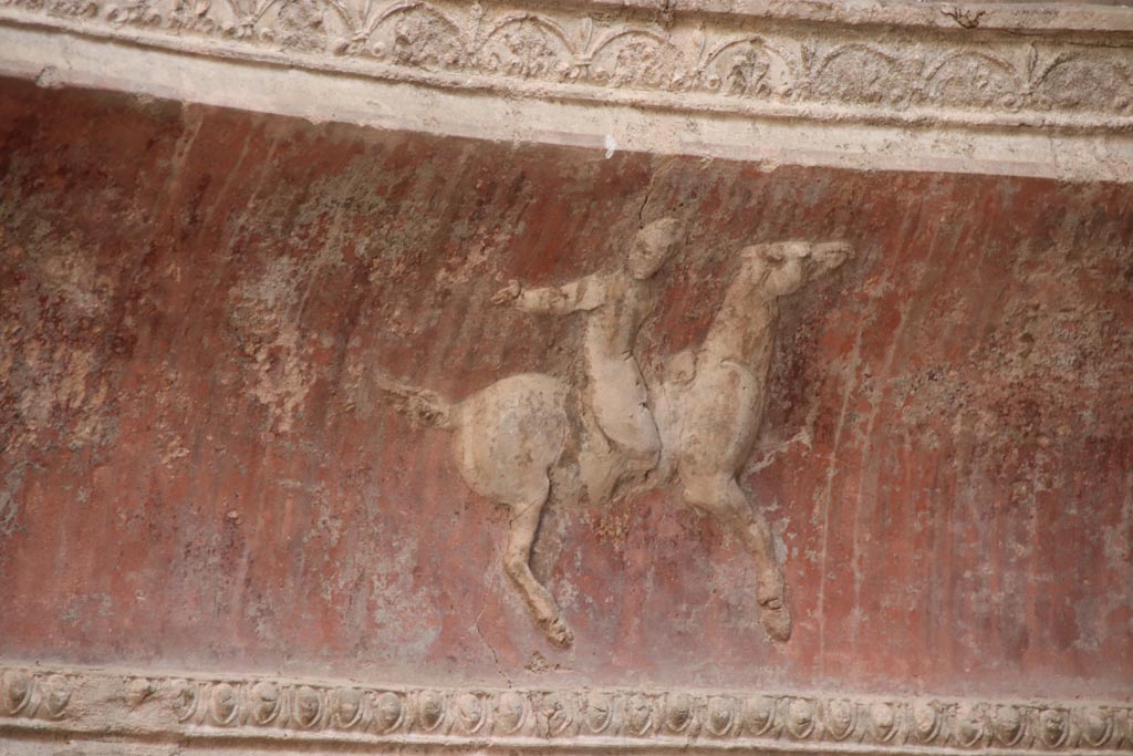 VII.5.24 Pompeii. October 2023. Frigidarium, detail of plasterwork showing a cupid on horseback. Photo courtesy of Klaus Heese.