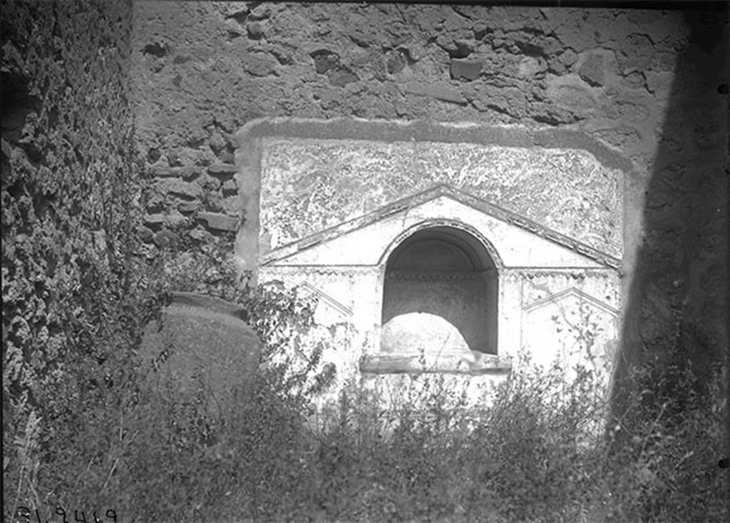 VII.15.8 Pompeii, 1931. Looking towards niche in north wall of garden area. 
DAIR 31.2462. Photo © Deutsches Archäologisches Institut, Abteilung Rom, Arkiv. 
According to Boyce, in the centre of the north wall of the garden area near the floor, was an arched niche.
The wall around it was covered with a rectangular panel of white stucco.
On this was an aedicula façade which was marked off with yellow and violet lines in low relief.
The work was delicately executed but somewhat irregular.
See Boyce G. K., 1937. Corpus of the Lararia of Pompeii. Rome: MAAR 14. (p.72, no.332, Pl.6,2) 
