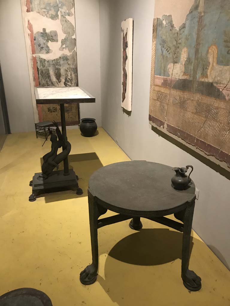 VII.16.17-22 Pompeii. April 2019. On display in Antiquarium, from House of Fabius Rufus. 
Bronze table with cupid riding a dolphin and marble top. PAP inventory number 13371.
Bronze table with lion's feet. PAP inventory number 13108.
On table is a bronze pitcher with face of a follower of Dionysus. PAP inventory number 14072.
Photo courtesy of Rick Bauer.
