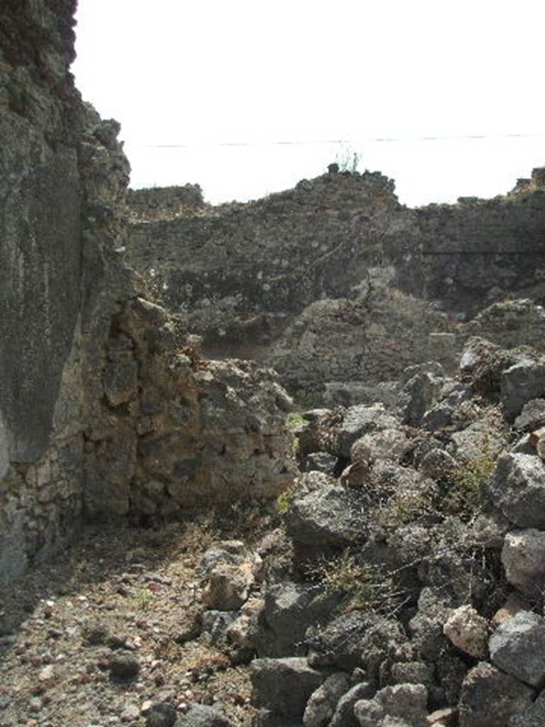 IX.6.5 Pompeii. May 2005. Looking south in room “l” (L) on south side of atrium. Over the ruined wall, the house at IX.6.4 can be seen.  (The pile of stones may be the remains of a staircase to the upper floor.) According to Mau, from room “L” one entered the stairs that leaned against the wall of “m” leading to the upper floor, whilst the stairs in “i”, as we have seen, communicated only with the upper rooms of IX.6.4, both not excavated.  
See Mau, in BdI, 1880, (p.228)
