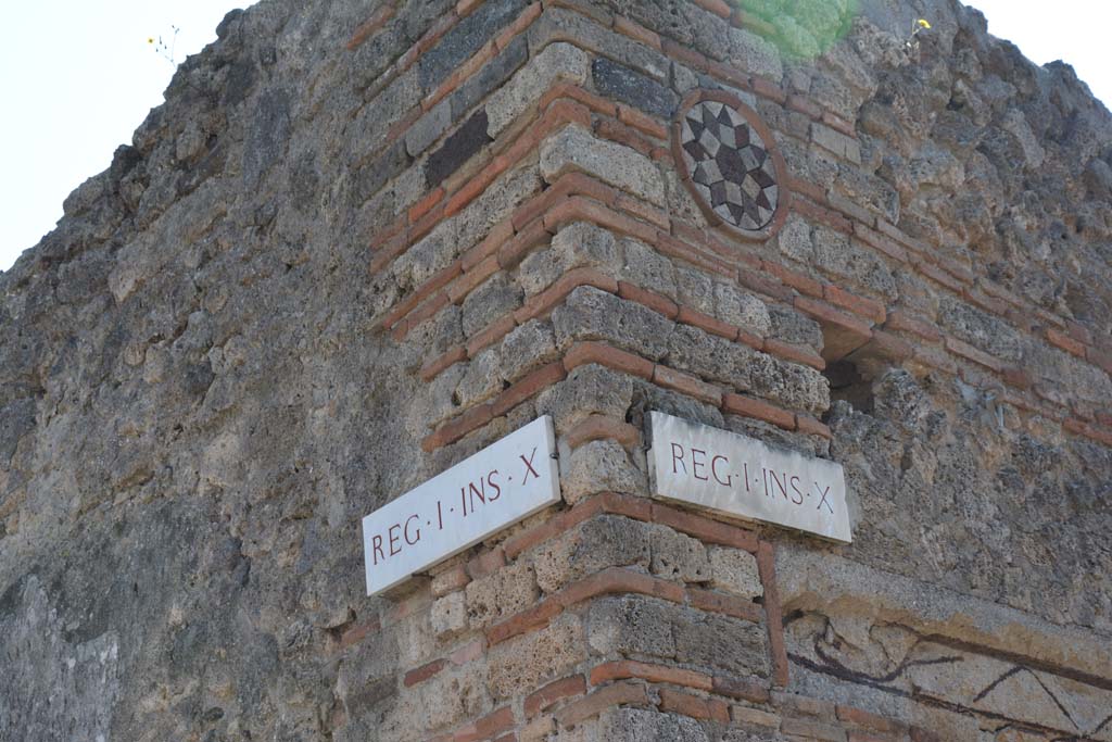 Vicolo del Citarista, April 2017. 
Corner of insula I.10, Vicolo del Menandro, on left, and coloured terracotta plaque above doorway of I.10.9, in Vicolo del Citarista, on right.  
Photo courtesy Adrian Hielscher.

