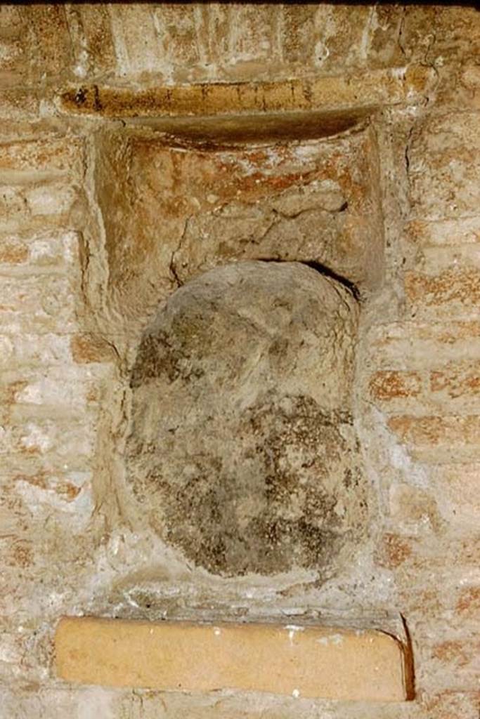 Street altar outside I.12.5, Pompeii. 1959. Photo by Stanley A. Jashemski.
Source: The Wilhelmina and Stanley A. Jashemski archive in the University of Maryland Library, Special Collections (See collection page) and made available under the Creative Commons Attribution-Non Commercial License v.4. See Licence and use details.
J59f0549
                            
According to PPM, inserted in the rectangular niche on the left side of the doorway was a blue lava stone, which had been a �lava-bomb� erupted during a prehistoric eruption and which was supposed to have been attributed with sacred and magical values. 
This was inserted into an apsed rectangular niche, with the lower level consisting of a tile projecting by about 6 cm and closed into the upper area by another tile with architrave under a flat arch in brick. 
See Carratelli, G. P., 1990-2003. Pompei: Pitture e Mosaici. Vol. II.  Roma: Istituto della enciclopedia italiana. (p.736)



