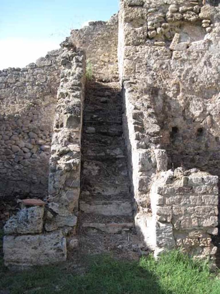 1.2.6 Pompeii. September 2010. Looking north to steps to upper floor, from north portico. 
On the right is the arched niche in the north wall of the kitchen on the upper floor. Photo courtesy of Drew Baker.
According to Boyce –
“In a small room, perhaps a kitchen on the intermediate floor, reached by stairs on north side of peristyle, was a Lararium.  
Below a small arched niche, a rectangular panel was marked off and within it was painted a single serpent advancing left towards the offerings upon an altar: in the background were plants and across the top were festoons.”
See Boyce G. K., 1937. Corpus of the Lararia of Pompeii. Rome: MAAR 14. (p.21 no.5).
Note: Found in the kitchen located on the first floor was a bronze statuette of Diana with bow and quiver. Giornale degli Scavi, N.S. III, 1874, 58.
See Giacobello, F., 2008. Larari Pompeiani: Iconografia e culto dei Lari in ambito domestico. Milano: LED Edizioni, (p.132, no.3)

