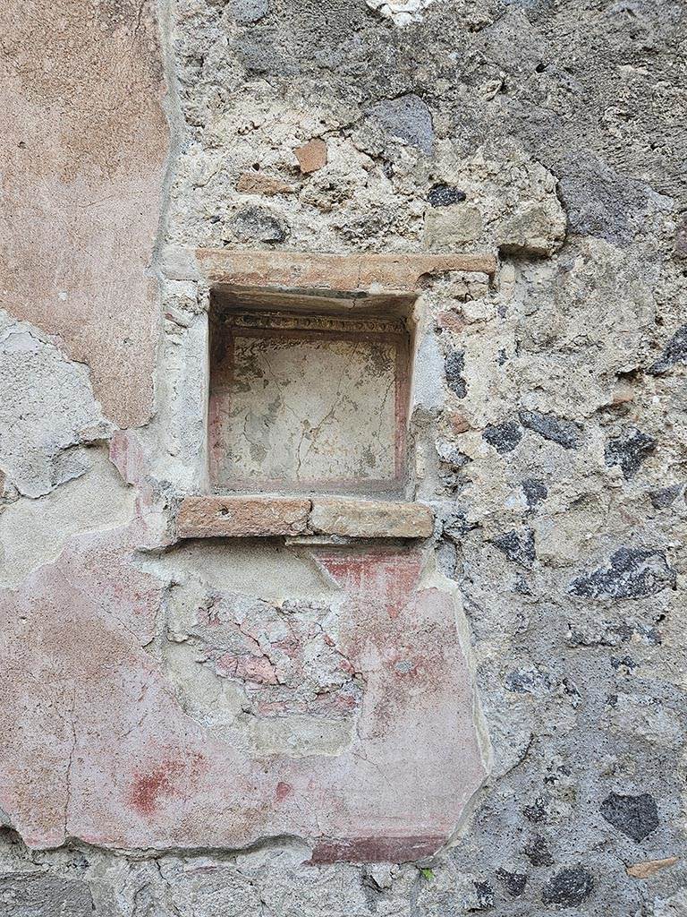 II.2.3 Pompeii. November 2024. East wall with square niche. Photo courtesy of Annette Haug.
According to Boyce, in the east wall was a square niche with heavy projecting ledge.
Its inside walls were white, bordered in red and around the top of the inside ran a stucco cornice.
A similar cornice ran around three sides of wall outside of the niche, to judge from the one side where the plaster was preserved.
On the edge of the projecting shelf was a graffito.
See Della Corte, M., 1965. Case ed Abitanti di Pompei. Napoli: Fausto Fiorentino. (p.379, CIL IV 8489)
See Boyce G. K., 1937. Corpus of the Lararia of Pompeii. Rome: MAAR 14. (P.30, no.63, Pl.4, 3, the location given as II.v.3)

According to Epigraphik-Datenbank Clauss/Slaby (See www.manfredclauss.de) this read as

Oliva condita
XVII K(alendas) Novembres      [CIL IV 8489]
