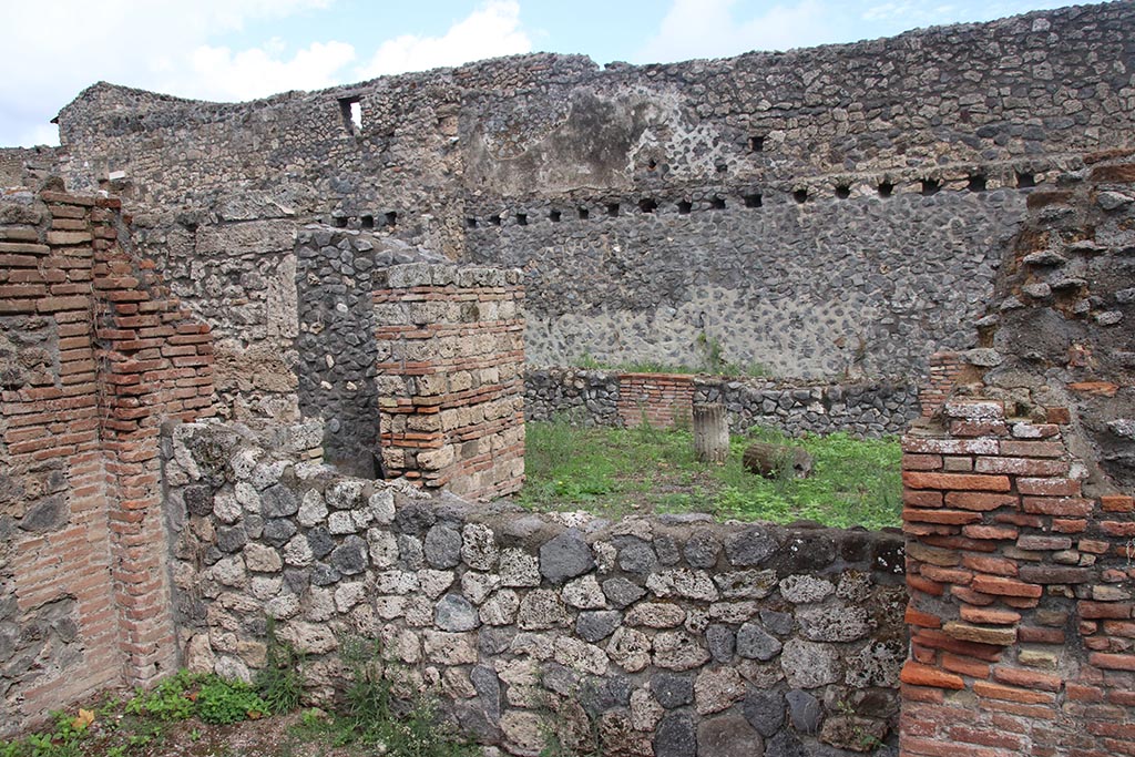 I.1.4 Pompeii, October 2024. 
Looking east across rear wall of rear room of I.1.4, towards north side of yard “c”, with doorway into room “e”. Photo courtesy of Klaus Heese.
