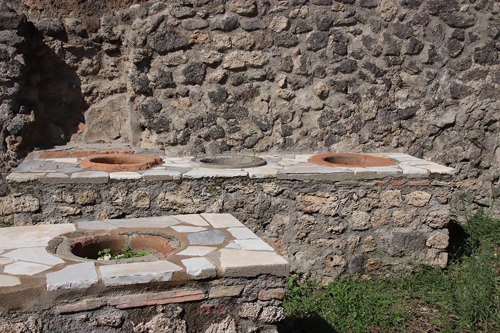 I.2.8 Pompeii. October 2024. 
North wall with niche behind additional counter with three urns, and L-shaped serving counter at the front. Photo courtesy of Klaus Heese.
