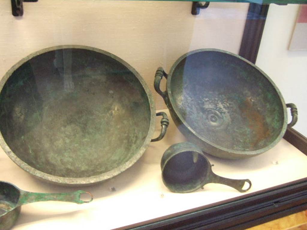 I.2.10 Pompeii. Found in Tablinum. (left rear) Bronze bowl. Now in Naples Archaeological Museum. Inventory number: 111554. (left front) Small Bronze saucepan. Now in Naples Archaeological Museum. Inventory number: 115975. Found in Tablinum. (right rear) Bronze bowl. Now in Naples Archaeological Museum. Inventory number: 111555. Found in Tablinum. (right front) Small Bronze saucepan. Now in Naples Archaeological Museum. Inventory number: 110061.