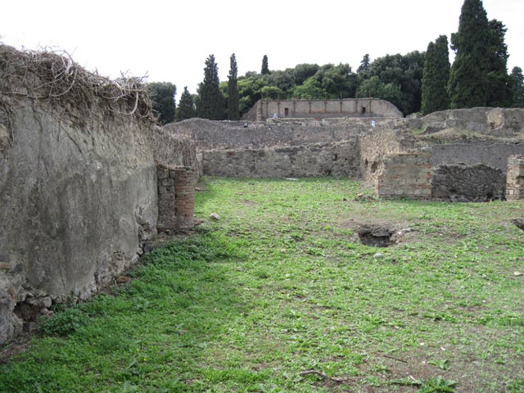 I.3.3 Pompeii. September 2010. Upper peristyle area, looking west towards the large exedra or triclinium, from the south-east corner. Photo courtesy of Drew Baker.
According to Warscher this was �triclinium �n�, south-west of the peristyle. She wrote �
�Nel pavimento cio� si vede un ornamento di forma quadrata, formato di pietruzze bianche, che non stando nel bel mezzo, ma pi� nell�interno della camera non poteva servir ad altra se non a segnar il posto ove fra letti si metteva la tavola.
Qui per� non stavano che due letti, i cui posti bene si riconoscono dal pavimento meno consumato. Nel muro N e verso S vi sono fori per lasciar scolare l�acqua. Le pareti sono decorate in nero con ornamenti architettonici nel terzo stile di Pompei (Giorn.Sc II, p.452 segg). Il quadro che in parte distrutto vi si trova fu descritto da me e spiegato per Ippolito con la nutrice nel Bull. 1873, p.273. Poi seguiva verso N un corridoio obbliquo che dirigendosi verso l�atrium conduceva alle stanze superiori. Ma di questo corridoio nulla � rimasto: si riconosce soltante dalle buche de� travi che lo sorreggevano�� (see photograph no.1, at I.3.1)
See Warscher, T, 1935: Codex Topographicus Pompejanus, Regio I, 3:  Rome, DAIR.  
(translation:  "In the floor one could see a square-shaped ornament that was formed from white stones, that were not in the beautiful middle, but more in the inside of the room where they could only serve as a sign to show the place where one put the table, between the couches. Here, however, there were only two beds, their place known well from the floor less worn.  In the north wall and towards the south, there were holes to let the water drain. The walls were decorated in black with architectural ornaments in the Third Style of Pompeii (Giorn.Sc II, p.452 following). The picture found here that was partly destroyed, was described by me and explained as Hippolytus with the nurse, in Bull. 1873, p. 273. Then followed towards the north, a sloping corridor that pointed towards the atrium leading to the upper rooms. But nothing remained of this corridor: one can recognize only the holes of the beams that supported it ... " (see photograph no.1, at I.3.1).

