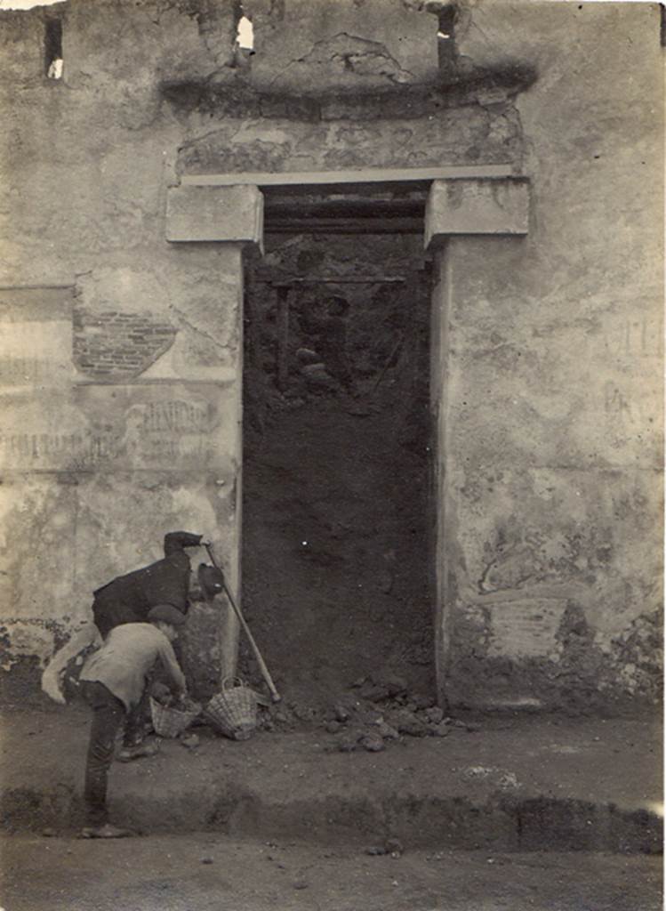 I.I.7.1 Pompeii. 6th January 1923. Entrance during excavation. Visible on each side of the doorway are the remains of electoral recommendations. Photo courtesy of Drew Baker. According to Varone and Stefani, immediately to the left of the door were a large number of electoral recommendations. To the right of the door were the electoral recommendations CIL IV 7196-8. See Varone, A. and Stefani, G., 2009. Titulorum Pictorum Pompeianorum, Rome: L�erma di Bretschneider. (p. 74

The remains of CIL IV 7212, CIL IV 7215, CIL IV 7210 (left) and CIL IV 7196 and 7197 (right) can be seen in this photograph. 

According to Epigraphik-Datenbank Clauss/Slaby (See www.manfredclauss.de) these read as:

Veientonem
aed(ilem) Primanus rog(at)       [CIL IV 7212]

L(ucium) Albucium
aed(ilem) o(ro) v(os) f(aciatis)      [CIL IV 7215]

L(ucium) Popidium Ampliatum
aed(ilem) Paquius rog(at)      [CIL IV 7210]

C(aium) Lollium Fuscum
aed(ilem) o(ro) v(os) f(aciatis)       [CIL IV 7196 ]

P(ublium) Paquium Proculum
[du]umvirum i(ure) d(icundo) vicini cupidi faciunt       [CIL IV 7197]

