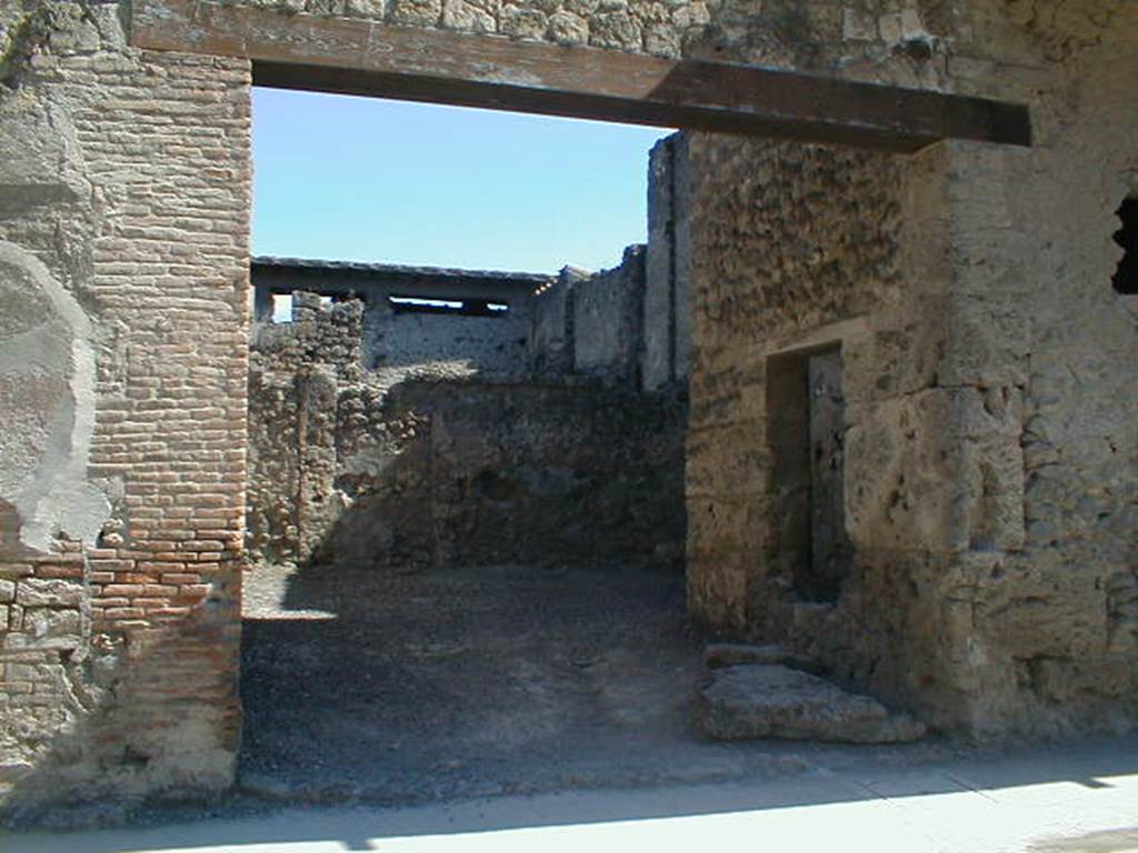 I.7.4 Pompeii. May 2005. Entrance on Via dell�Abbondanza. According to Maiuri, the workshop comprised of a large room on the ground floor, and a smaller room in the north-west corner. This smaller room had a small window in its north wall, onto the roadway, as well as a larger window in its east wall overlooking the vestibule of the workshop. 
Against the west perimeter wall was a masonry kitchen area. Found between the kitchen and the rear wall was the recognisable threshold step and traces in the plaster work of a long and steep wooden stairway that would have led up to the upper floor of the room, and from this led both to the balcony and to the other rooms on the upper floor which covered all the space on the ground floor, where there is no trace of an impluvium or possibility of water drainage. Therefore, the roof would have been totally closed and probably only one layer facing the roadway.  The walls of the ground floor were simply plastered with a clear yellow background with simple red lines forming squares.
See Maiuri, A., 1928. Nuovi Scavi nella Via dell�Abbondanza. Milano: Hoepli. (p.15-16).
