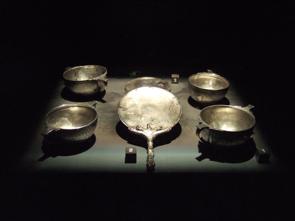 I.8.14 Pompeii. Silver found in the vestibule, probably kept in a wooden box. 
Four cups each with double handle, SAP inventory numbers 7484-7487.
Mirror with club or cudgel handle SAP inventory number 7480.
Another round mirror with corrosion and perforation, SAP inventory number 7479.
See Guzzo, P. (A cura di), 2006. Argenti a Pompei. Milano, Electa. (p. 149-150).
