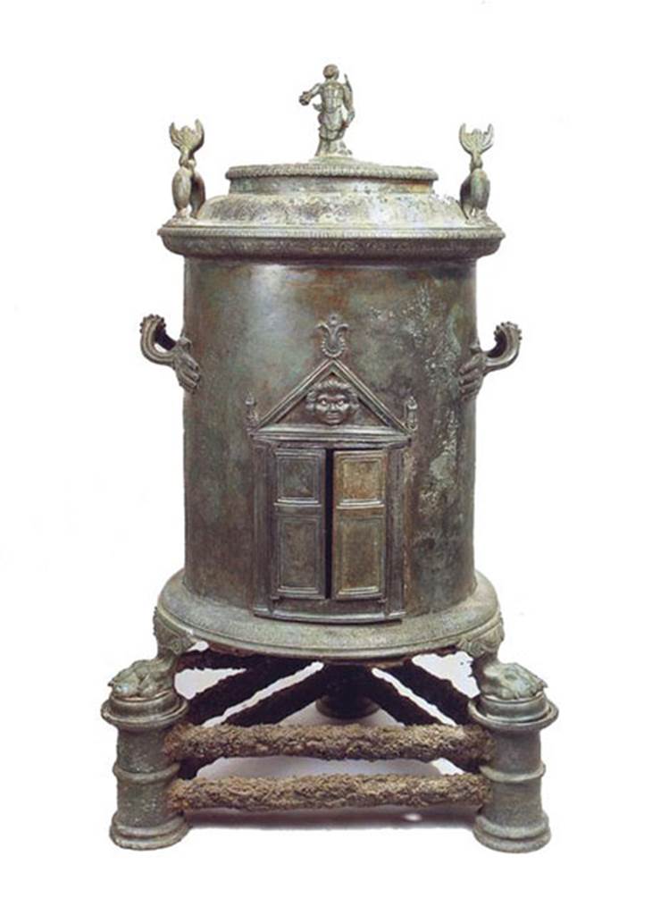 I.8.17 Pompeii. Bronze cylindrical food warmer found in a made to measure niche under the stairs in the servants’ quarters.
It has a lid with three handles, one in the form of a statuette of Triton in the centre and two dolphins at the edges.
On the body are two handles in the form of hands, double doors at the front are surmounted by a pediment with palm leaves and a Medusa's head.
At the base, lion’s paw feet rest on three pillars connected by a double iron bar.
Now in Naples Archaeological Museum. Inventory number 6798.
See Conticello, B., Ed, 1990. Rediscovering Pompeii. Rome: L’Erma di Bretschneider, p. 173, no. 59.