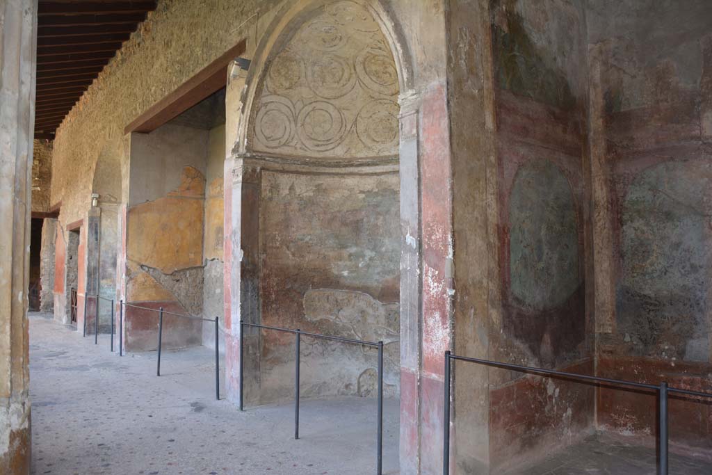 I.10.4 Pompeii. September 2019. Looking towards south side of south portico, from south-west corner.
On the right is Alcove 25 (Sacrarium), followed by Alcove 24, 23, and 22 and doorway to 21, in south-east corner.
Alcove 24 has a domed top decorated with stucco, underneath which is a painting of Venus and cherubs in a temple.
Alcove 23 has the painting of the seated poet Menander. 
Alcove 22 also has a domed top decorated with stucco, underneath which is a painting of Diana and Acteon.
Room 21 has a mosaic emblema of satyr and maenad in the centre of the mosaic floor.
Foto Annette Haug, ERC Grant 681269 D�COR.


