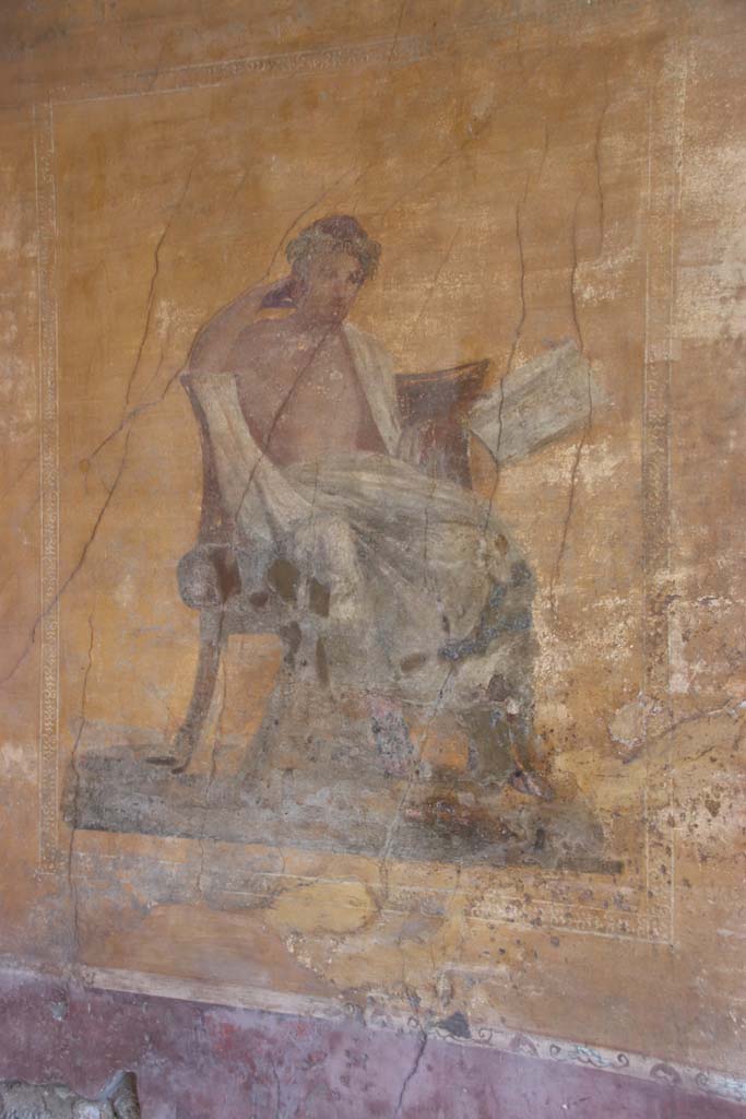 I.10.4 Pompeii. September 2021. 
Alcove 23, west wall with wall painting of a seated poet. Photo courtesy of Klaus Heese.
The name of Menander was inscribed by the painter on the skirt of the man�s cloak. 
In this alcove there are also painted masks, with possibly Bacchus sitting on a chair with a robe covering his legs, and a painted table.

