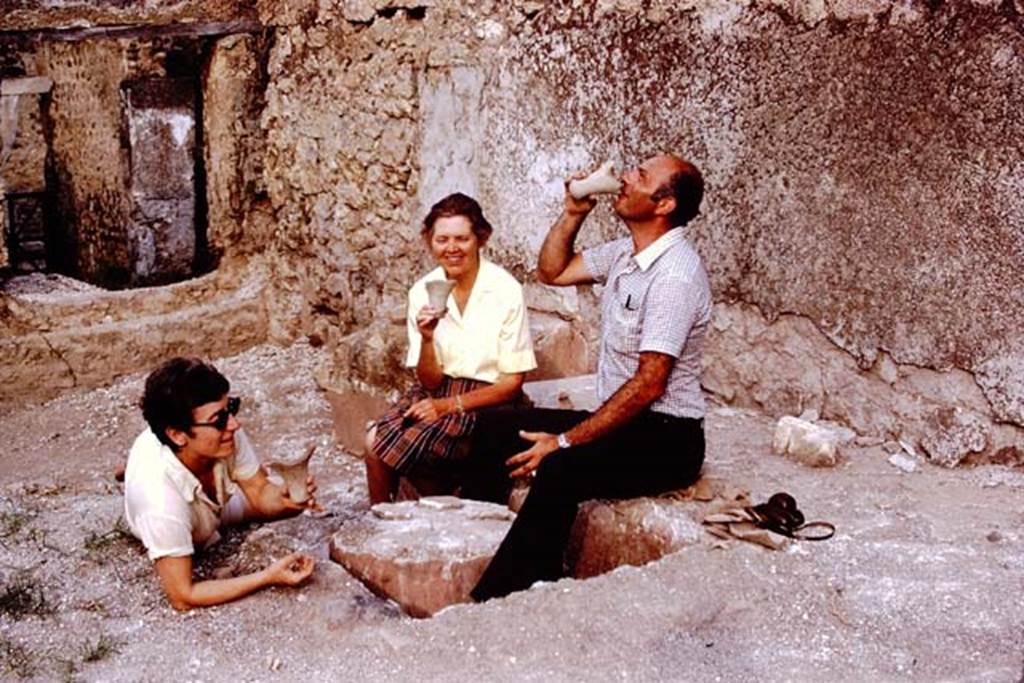 I.14.2 Pompeii. 1972. Looking south-east across the triclinium towards the entrance doorway in the atrium, on left. Photo by Stanley A. Jashemski. 
Source: The Wilhelmina and Stanley A. Jashemski archive in the University of Maryland Library, Special Collections (See collection page) and made available under the Creative Commons Attribution-Non Commercial License v.4. See Licence and use details.
J72f0340
According to Wilhelmina, �substantial amounts of original lapilli had been left along the south wall of the garden area. In the south-east corner of the garden was the triclinium, smaller than most, and two tables still covered by original lapilli. Between the couches was a round table, whereas the one against the south wall was a rectangular one. Two of Wilhelmina�s students happily posed on the triclinium, waiting to be served.�  
