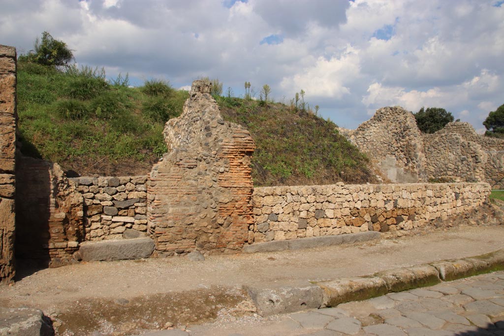 III.7.4 Pompeii, on left. October 2022. Entrance doorway, with grey lava doorway threshold under new wall, on north side of Via dell’Abbondanza.
Centre right can be seen another wider grey lava doorway threshold belonging to III.7.5.  
Continuation of front façade wall from previous photos in III.7.1, 2 and 3. Photo courtesy of Klaus Heese.
