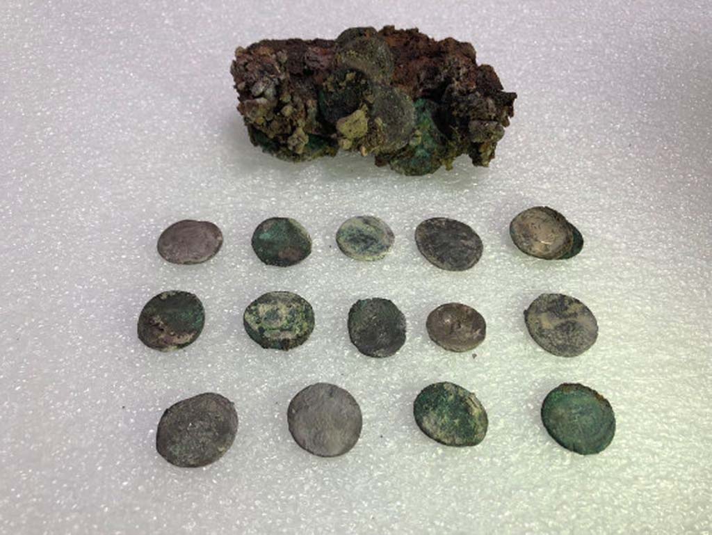 Regio V Pompeii. 2018. Leather pouch containing coins found under Pompeii skeleton in the Vicolo dei Balconi.
At first examination of the money found with skeleton of victim there would seem to be at least 20 silver denarii and two bronze asses for a nominal value of eighty sesterces and a half. 
Such a quantity of coins could at that time ensure the maintenance of a three-person family for 14, 16 days. 
The coins have very varied chronology. 
It was possible to examine 15 coins, for the main part Republican, starting from the Mid-second century B.C. 
One of the later Republican coins is a legionary denarius of Mark Antony, common in Pompeii, with the indication of the XXI Legion. 
Among the few Imperial coins identified, a probable denarius of Octavian and two denarii of Vespasian.

Borsa di cuoio contenente monete trovate sotto lo scheletro di Pompei nel Vicolo dei Balconi.
Al primo esame delle monete trovato con lo scheletro della vittima sembrerebbero esserci almeno 20 denari d'argento e due as di bronzo per un valore nominale di ottanta sesterzi e mezzo.
Una tale quantit� di monete potrebbe quindi garantire il mantenimento di una famiglia di tre persone per 14, 16 giorni.
Le monete hanno una cronologia molto varia.
Fu possibile esaminare 15 monete, per lo pi� repubblicane, a partire dalla met� del II secolo a.C.
Una delle monete repubblicane pi� tardi � un denario legionario di Marco Antonio, comune a Pompei, con l'indicazione della XXI Legione.
Tra le poche monete imperiali identificate, un probabile denario di Ottaviano e due denari di Vespasiano.

Photograph � Parco Archeologico di Pompei.
