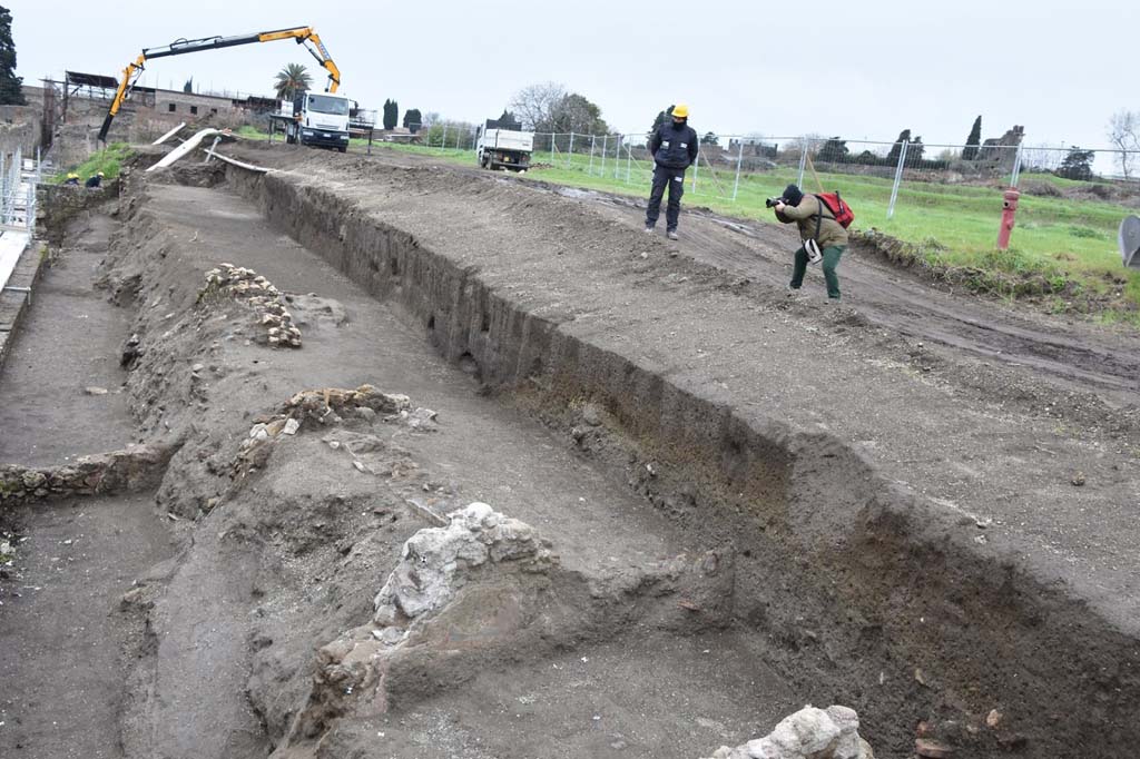 South side of Reg. V.7 near V.7.7 Pompeii. 2018. Start of excavations, uncovering the tops of walls. Looking west towards the upper floor of the House of the Vettii.
Photograph © Parco Archeologico di Pompei.

