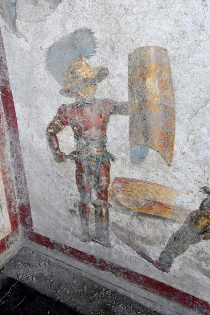 Detail of the "Mirmillo" of the "Scutati" category: he wields the offensive weapon, the gladium, (short Roman sword) and a large rectangular shield (scutum) and wears a wide-brimmed helmet equipped with visor with plumes, the cimian. 

Dettaglio del “Mirmillone” della categoria degli "Scutati”: impugna l’arma di offesa, il gladium, (corta spada romana) e un grande scudo rettangolare (scutum) e veste un elmo a tesa larga dotato di visiera con pennacchi, il cimiero.

Photograph © Parco Archeologico di Pompei.
