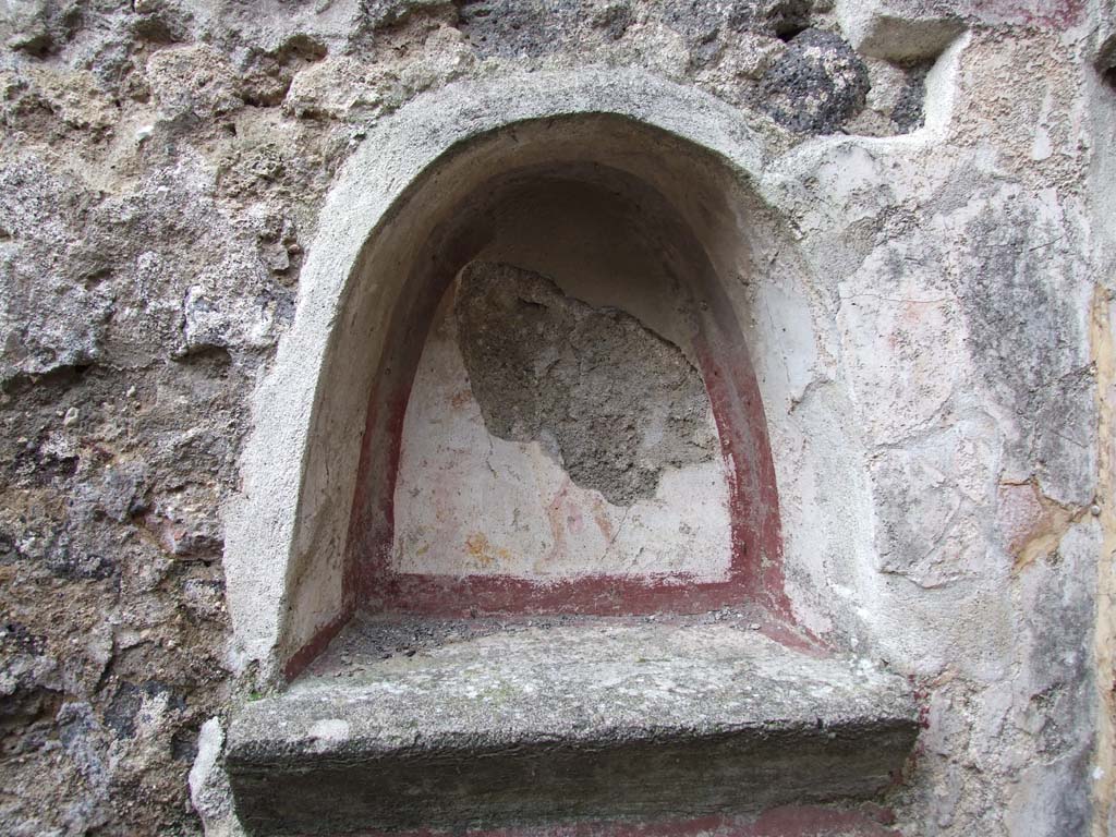 VI.7.23 Pompeii. December 2006. Kitchen, niche above household altar on north wall of kitchen.
According to Boyce, the inside walls were coated with white stucco, the corner outlined with broad red stripes.
Beneath it the floor projects from the surface of the wall.
On the back wall of the niche was painted the figure of the Genius, holding a patera with his right hand above a flaming altar.
The wall around the niche was covered with a panel of the same white stucco, bordered in red.
On each side of the niche was painted a Lar in yellow tunic and red pallium.
See Boyce G. K., 1937. Corpus of the Lararia of Pompeii. Rome: MAAR 14. (p. 48, no. 167, and Pl. 11,1)