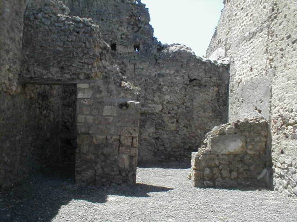 VI.14.24 Pompeii. May 2005. Looking west across shop to doorways to two rear rooms.
According to BdI, on the right of the shop entrance in the north-east corner, was a small hearth, and in the same corner was a latrine. Objects found in the shop were a bell, various pots, five keys and a few bronze coins. The rear room on the right was the biggest. 
Upon excavation, the walls of the upper rooms were also preserved, one above the rear rooms, the other above the shop-room. This last wall, with pink coloured plaster until the height of approximately 1.50m, unpainted above, and with a large window onto the roadway.  It was evident that these two rooms joined by a doorway between them, formed a separate complex from the rest of the house, and that this could be rented independently from the shop below. See Bullettino dell�Instituto di Corrispondenza Archeologica (DAIR), 1876, (p.44)
