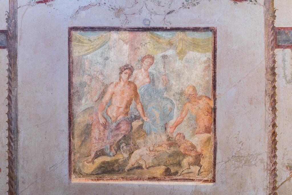 VI.15.1 Pompeii. March 2023.
Central wall painting on south wall showing Dionysus and Ariadne, as well as the fight between Eros and Pan.
Photo courtesy of Johannes Eber.
Kuivalainen comments –
“A young half-naked Bacchus in the company of Ariadne, watching the fight about to begin, and Silenus already preparing to reward the victor with the palm leaf. The female figure’s dignified appearance suits Ariadne more than a maenad. His identification is also supported by her embracing arm. This motif of a fight between a cupid and a faun appears elsewhere as well; a good example is an outdoor scene from Herculaneum.” (MANN 9262).
See Kuivalainen, I., 2021. The Portrayal of Pompeian Bacchus. Commentationes Humanarum Litterarum 140. Helsinki: Finnish Society of Sciences and Letters, (p.133-35, D13).