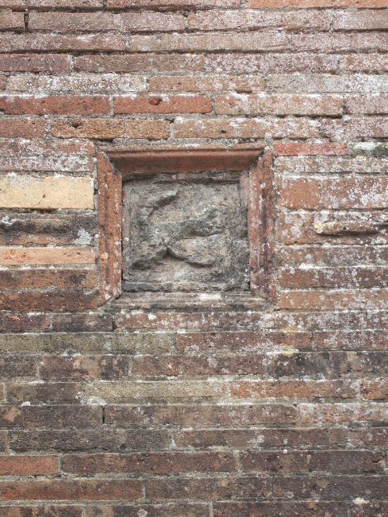 VII.2.32 Pompeii. May 2006. Plaque showing a flying phallus, on wall between VII.2.31 and VII.2.32. According to Della Corte, �a characteristic, complex relief (embedded in the wall to the left of the first entrance) destined to protect the hostelry�.  

