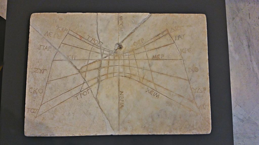 VII.4.57 Pompeii. November 2018. According to the information card –
“The sundial was discovered at Pompeii on 14th July 1837 in the House of the Figured Capitals.
The dial consists of a portion of an oblique circular cone.
The lower curve corresponded to the dates of 30 April and 12 August since the dial erroneously terminates before the extension it ought to have had to capture the shadow cast by the gnomon at the summer solstice.
There are 11 engraved hour lines: in accordance with the standard layout, the lines are made by joining the edges of the 12 respective parts into which the three day curves are divided.”
On display in Naples Archaeological Museum. Photo courtesy of Giuseppe Ciaramella.