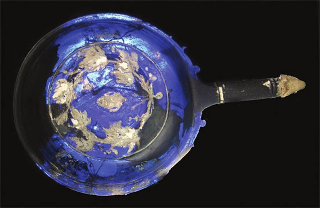 VII.4.62 Pompeii. Tablinum 8, cameo glass patera. The interior of the Patera in white decoration shows a sacred knot with bunches of flowers and sacred ribbons. It was found scattered in many fragments near the room to the right of the tablinum of VII.4.59 Casa della Parete Nera and the room of the adjoining VII.4.62 Casa delle Forme di Creta. Now in Naples Archaeological Museum.  Inventory number 1843.
