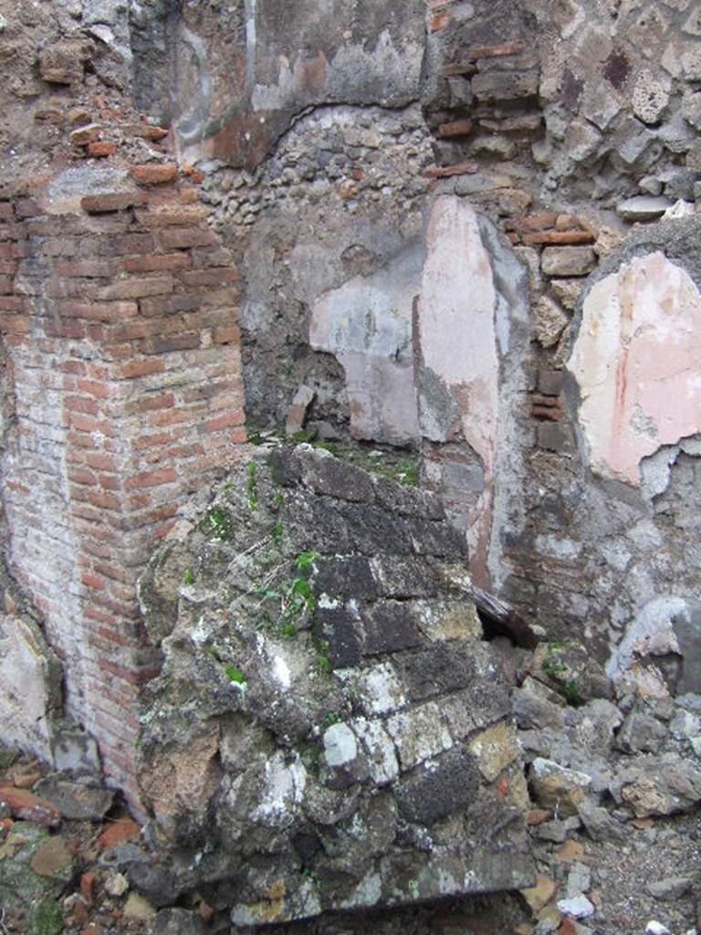 VII.10.3 Pompeii. December 2005. Doorway to room 4, in north-west corner of atrium.
The doorway would have led into a room, described as a triclinium, originally with flooring of a reddish cocciopesto. The door threshold was formed by two square slabs of travertine and inserted in its south end was a small slab of grey marble. Seen on each of the smooth surface of the slabs, was a circular recess for the fixing of the double-door hinges. (p.54)
The floor was upgraded to a black and white mosaic. The walls were redecorated in the IVth style. The black zoccolo (dado/plinth) showed alternative narrow panels with rosettes, in the centre were plants motifs. The middle zone on each wall showed an edicula panel, painted white which contained a pinax, no longer visible. The side panels were painted red, edged by a simple bordered band.
Studi della Soprintendenza archeologica di Pompei, 22: l”Insula VII, 10 di Pompei, by Angelo Amoroso, (p.54 and p.74) 

According to Bragantini, on the north-east side the mosaic was visible, whilst on the south-east side the cocciopesto was visible.
See Bragantini, de Vos, Badoni, 1986. Pitture e Pavimenti di Pompei, Parte 3. Rome: ICCD. (p.179)

