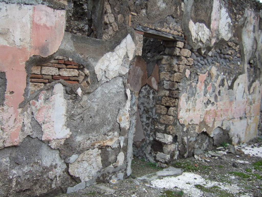 VII.10.3 Pompeii. December 2005. Doorway to room 6, a cubiculum on north side of atrium.
This room also had a floor of cocciopesto, joined in the doorway to the threshold which was formed by two rectangular travertine slabs, marked in the centre with a circular recess for the fixing of the double-door hinges.  When redecorated the walls were repainted with plaster panels edged with a red line, of which some traces remain.  The middle of the walls had vertical panels separated by architectural paintings, the central panels were yellow, the sides being red.  The zoccolo was painted with plant motifs on a red background.  The upper part of the walls was painted white. Its original flooring was kept.
Studi della Soprintendenza archeologica di Pompei, 22: l”Insula VII, 10 di Pompei, by Angelo Amoroso, (p.54 and p.74) 
