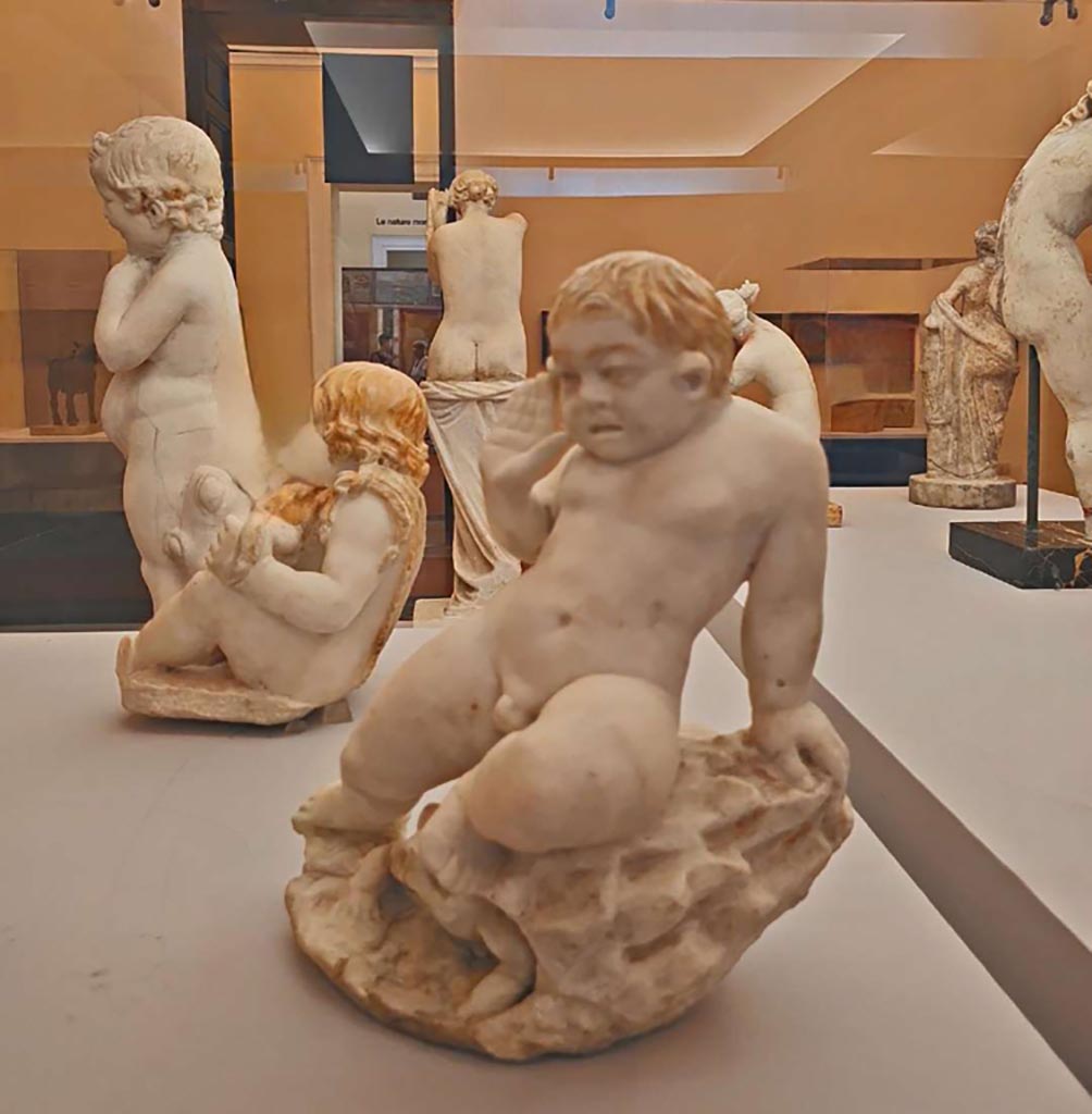 VII.12.23 Pompeii. October 2023. Two statuettes found in the garden area.
Centre left – (10) Fountain figure of child holding fruits in his mantle, (inv. 6500).
Centre right - (11) Fountain figure of a child frightened by a toad, (inv. 6537).
Photo courtesy of Giuseppe Ciaramella. 
On display in “L’altra MANN” exhibition, October 2023, at Naples Archaeological Museum.
