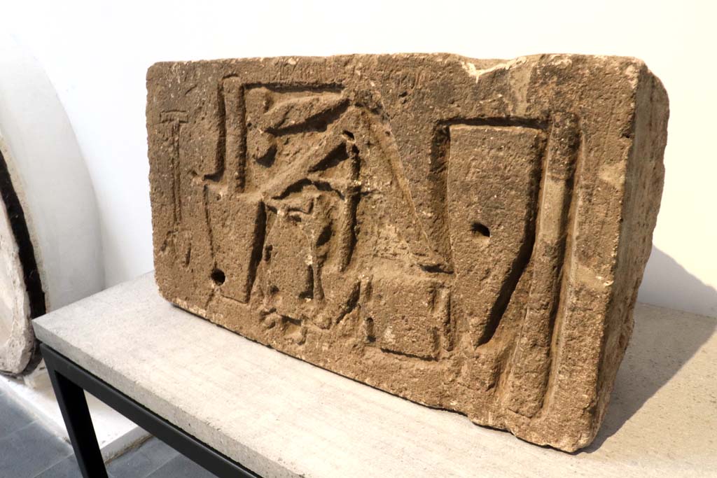 VII.15.1/2 Pompeii. February 2021.
Limestone relief signed by the master builder (structor) Diogenes depicting –
a trowel, an apotropaic phallus, a plumbline, a cudgel or an axe/a hammer that cuts orthogonally, a scalpel and two unidentifiable objects.
On display in Antiquarium at VIII.1.4, but found on the west perimeter wall of the house at VII.1.52, on Via dei Soprastanti.
Photo courtesy of Fabien Bièvre-Perrin (CC BY-NC-SA).