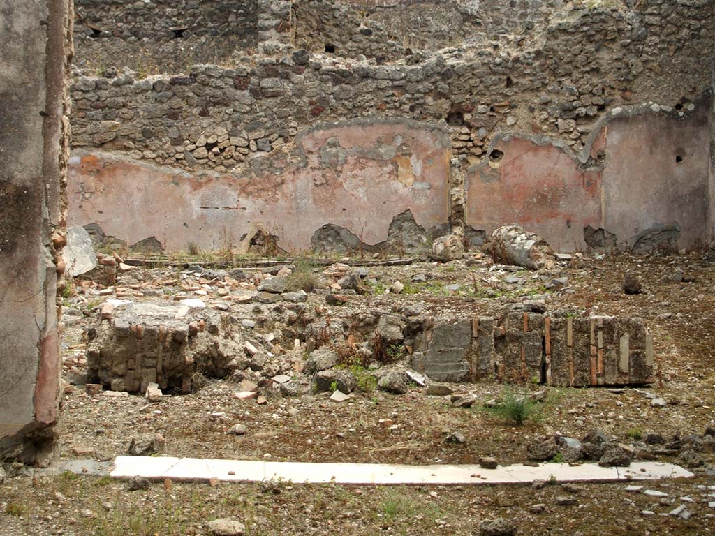 IX.5.18 Pompeii. May 2005. Looking east from triclinium room f, across atrium and pool, in atrium/courtyard b, with remains of a fallen column.
On the east side of the atrium, the rear (east) wall of room k (a narrow storeroom with stairs to the upper floor) can be seen on the left.
On the right, would have been the rear (east) wall of room i, a cupboard with holes for shelving supports.