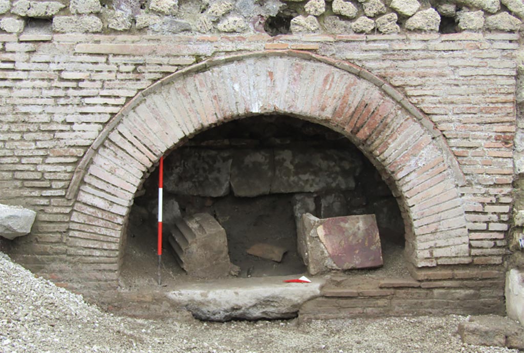 IX.10.1 Pompeii. December 2023. Oven 7a. Looking west to the oven front. 
The partially visible structures already suggested the presence of a production facility with an oven, a hypothesis that was confirmed when the burying material was removed. 
Along the north wall of oven 7a, a rectangular basin (ca. 1.50 x 0.80 m) was uncovered, the bottom of which has not yet been reached.
A significant feature of room 7 is the presence of two circular masonry structures, not entirely visible at present, on which the circular cones of two millstones must originally have rested, cones that are, however, not present on the bases. The condition of the excavation, which is still in progress, leads one to be cautious; however, it is legitimate to ask whether the absence of the millstones is attributable to removals that occurred during the 19th-century excavations.

IX.10.1 Pompei. Maggio 2023. Forno 7a. Vista verso ovest sul fronte del forno. 
Le strutture parzialmente a vista facevano già supporre la presenza di un impianto produttivo con forno, ipotesi che ha trovato conferma allorché si è proceduto alla rimozione dell’interro.
Lungo la parete nord del vano 7a si è messa in luce una vasca rettangolare (1.50 x 0.80 m ca.) di cui ancora non si è raggiunto il fondo.
Elemento significativo di ambiente 7 è la presenza di due strutture circolari in muratura, attualmente non del tutto visibili, su cui, in origine, dovevano poggiare le mete circolari di due macine, mete che però non sono presenti sulle basi. La condizione dello scavo ancora in fieri induce ad essere cauti, ad ogni modo è lecito domandarsi se la mancanza delle macine sia imputabile ad asportazioni avvenute durante gli scavi ottocenteschi.
Photograph © Parco Archeologico di Pompei.
Vedi/See Ri-scavare Pompei: nuovi dati interdisciplinari dagli ambienti indagate a fine ‘800 di Regio IX, 10.1.4. E-journal 2, Scavi di Pompeii, 29.5.2023, p. 4, fig. 3. E-journal on PAP web site 

