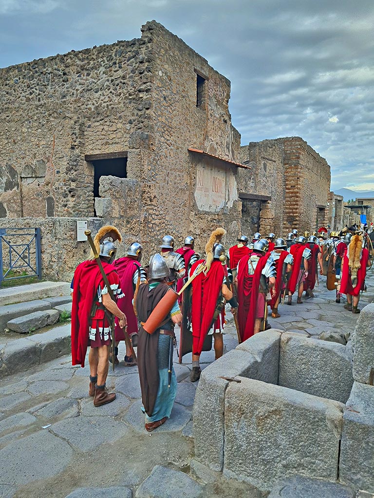 Via dell’Abbondanza, north side. 28th September 2024. Roman Legionary re-enactors marching.
Looking north-east towards III.2.1, on left, towards III.2.2 and III.2.3, on right, during “Ludi Pompeiani” event. 
Photo courtesy of Giuseppe Ciaramella.

