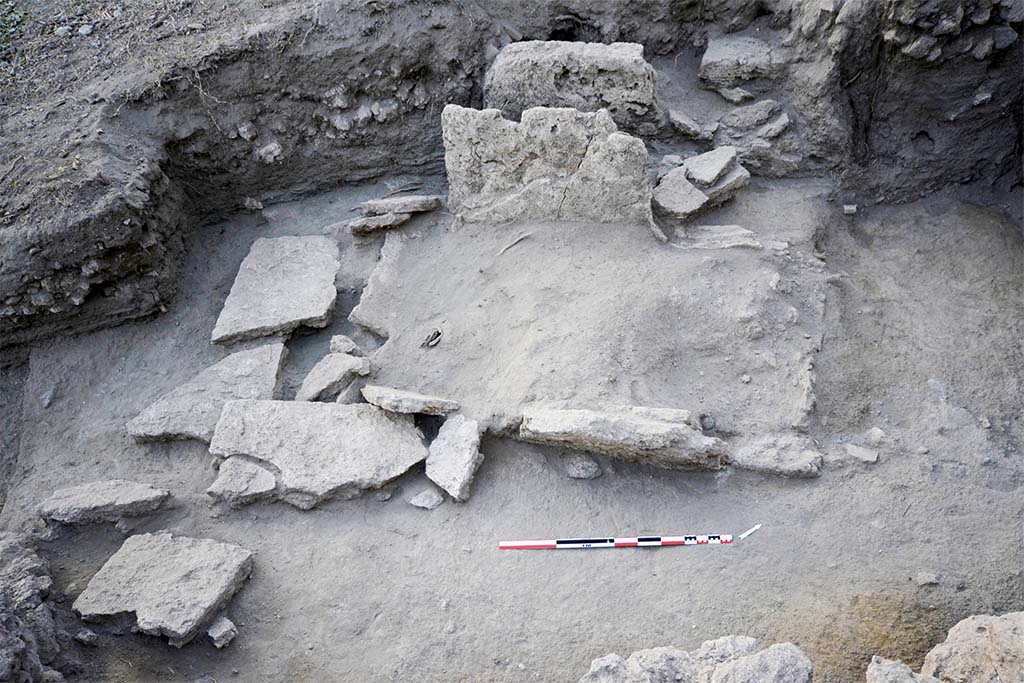 The collapsed slabs of burial SP30055 (HGE31A) being excavated. Taken from the east. 
Photo � B. Lemaire, EFR/CNRS. 
Burial SP30055, shows elements of the fractured and fallen wall slabs (Fig. 24). 
It was a box burial consisting of four monolithic slabs of Sarno limestone placed in the field, delimiting a space in which the deceased and the offerings were placed. 
The levels in place that have come down to us allow us to put forward the hypothesis that the burial is installed in the substratum, most probably with the digging of a pit whose limits are represented by the blocks forming the burial. 
The slabs on the short sides are enclosed by those on the long sides, forming a box and defining a rectangular structure of 2.25 m by 1.40 m (maximum), oriented north-east/south-west.
The north-western wall, which is better preserved (31.94 m s.l.m.), makes it possible to restore the height and thus the internal space of the tomb: 1.94 m by 0.98 m, for a height of 1.08 m.
(See CEFR 1581 and below) Para 42, Fig. 24.

Les dalles effondr�es de la s�pulture SP30055 en cours de fouille. Pris de l�est. 
Photo � B. Lemaire, EFR/CNRS. 
La s�pulture SP30055, pr�sente des �l�ments des dalles des parois fractur�es et tomb�es au sol (fig. 24). 
Il s�agissait d�une s�pulture � caisse mat�rialis�e par quatre dalles monolithes en calcaire du Sarno pos�es de champ, d�limitant un espace dans lequel sont install�s le d�funt et les offrandes. 
Les niveaux en place qui nous sont parvenus permettent d�avancer l�hypoth�se que la s�pulture est install�e dans le substrat, tr�s probablement avec le creusement d�une fosse dont les limites sont repr�sent�es par les blocs formant la s�pulture. 
Les dalles des petits c�t�s sont enserr�es par celles des grands c�t�s, formant un coffre et d�finissant une structure rectangulaire de 2,25 m sur 1,40 m (au maximum), orient�e nord-est/sud-ouest.
La paroi nord-ouest, mieux conserv�e (31,94 m s.l.m.), permet de restituer la hauteur et ainsi l�espace interne de la tombe : 1,94 m sur 0,98 m, pour 1,08 m de hauteur.
(Voir CEFR 1581 et ci-dessous) Para. 42, Fig. 24.
