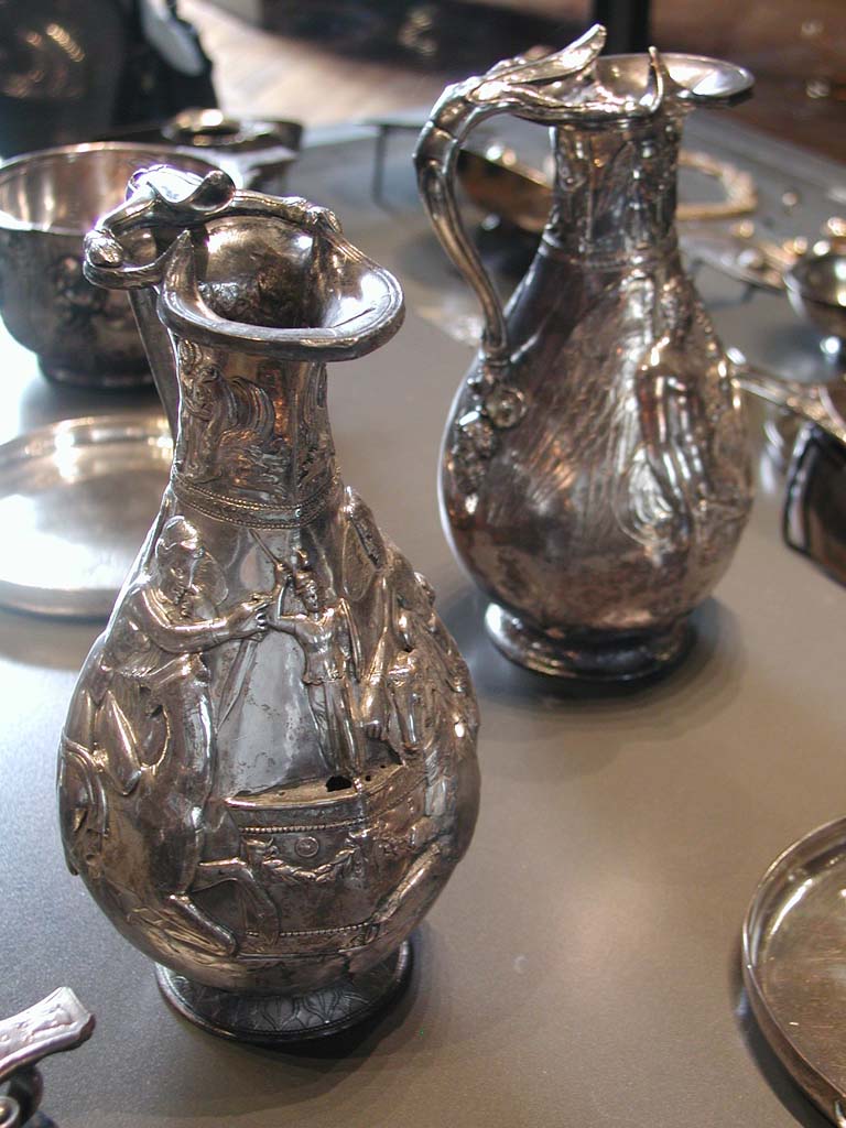 Villa della Pisanella, Boscoreale. Boscoreale Treasure. Front: Oenochoe, silver wine vase with repousse decoration and traces of gilding. Height about 25 cm. Side 1.
On the neck: a winged genius give water to a griffin. On the body: one victory sacrifices a deer.
Avant : Oenochoe du trésor de Boscoreale - Vase à vin en argent décors repoussé, traces de dorure. Hauteur environ 25 cm. Côté 1.
Sur le col : un génie ailé abreuvant un griffon. Sur la panse: une victoire sacrifie un cerf.
Now in the Louvre, inventory number BJ 1898.